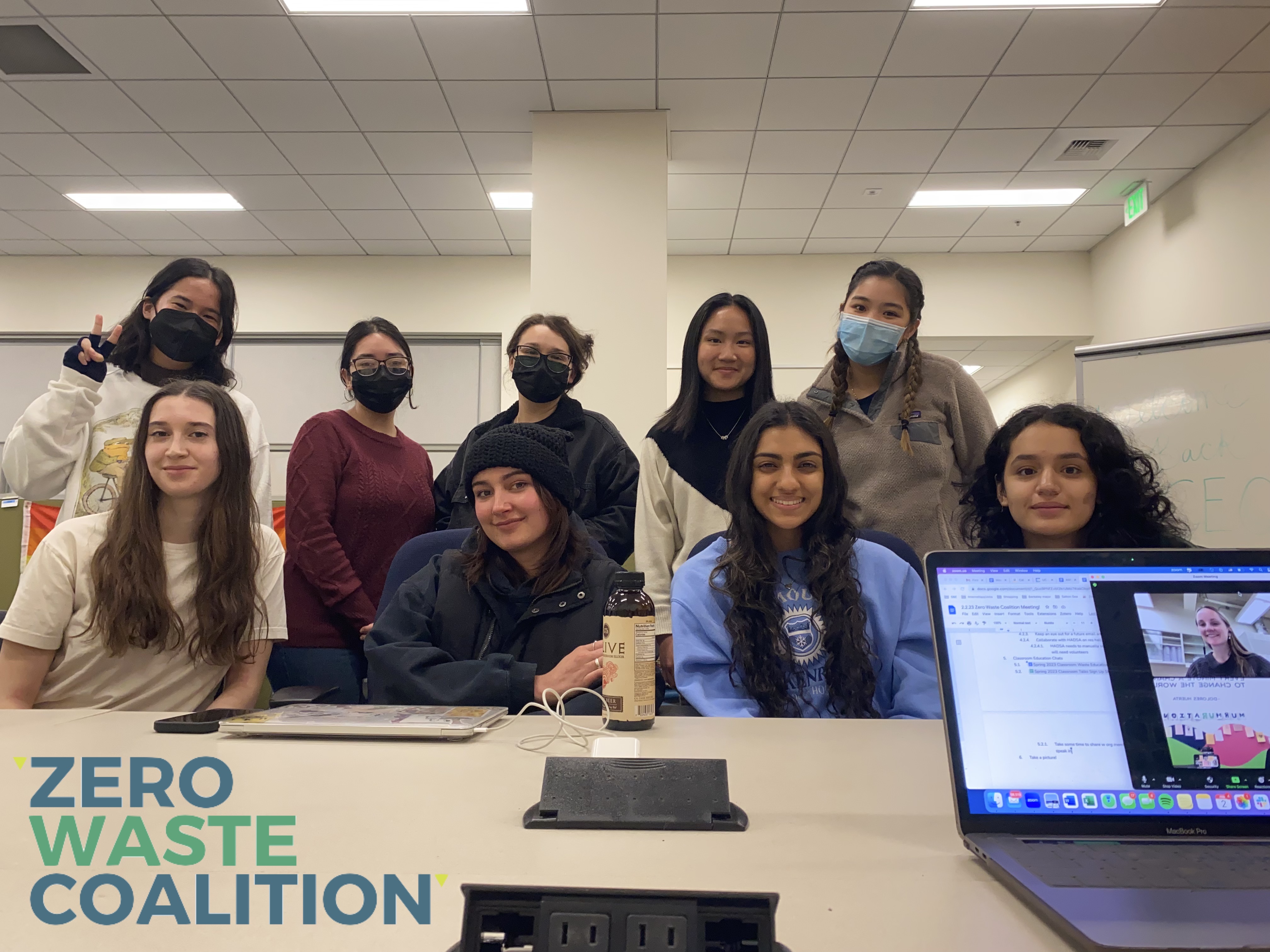 Photo of nine students smiling in the SERC Space with the Zero Waste Coalition logo in the left corner and a laptop with online members in the right corner