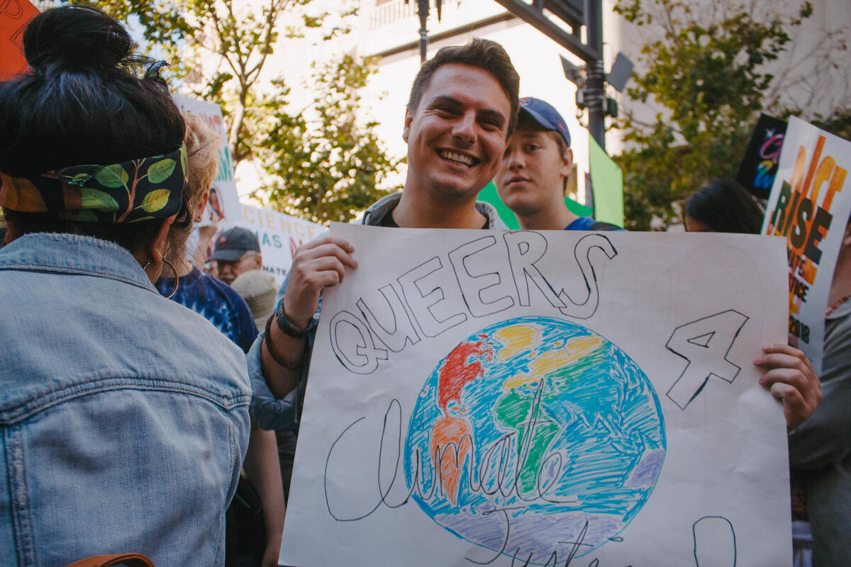 Brian Gialketsis holding a sign reading "Queers 4 Climate Justice."