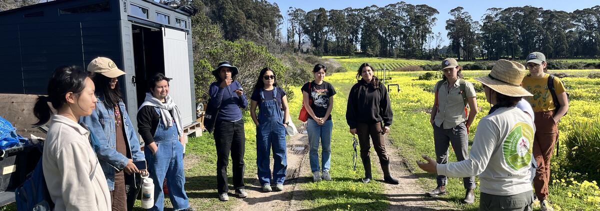 A group of people in a circle in front a green field